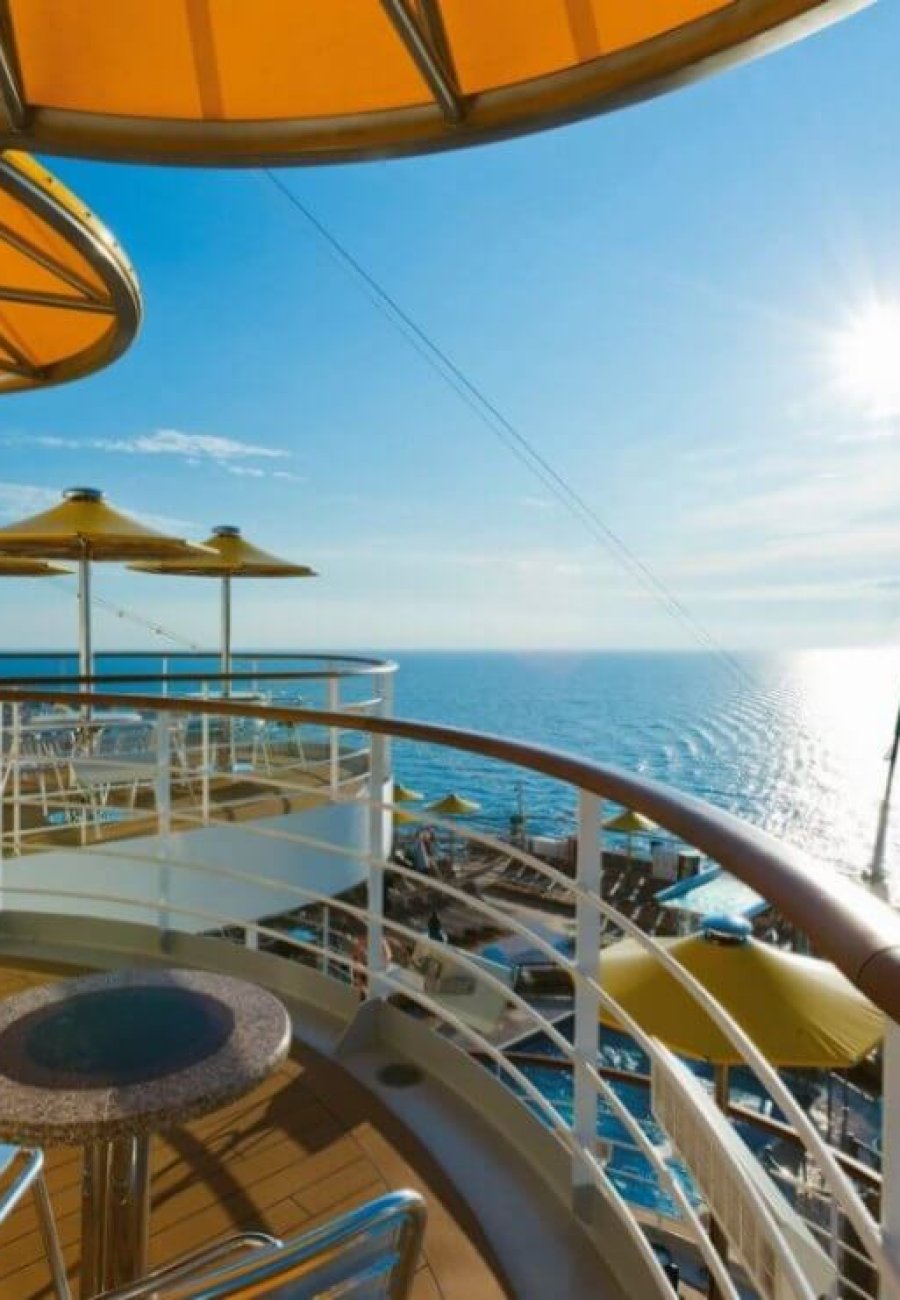 Sonnendeck der Costa Fascinosa mit Tischen, Stühlen, Sonnenschirmen und italienischer Flagge über dem Meer.