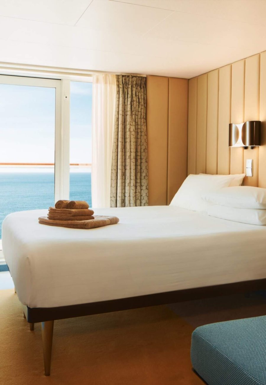 Helle Balkonkabine der Costa Smeralda mit Doppelbett, modernem Interieur und Meerblick durch die Balkontür.